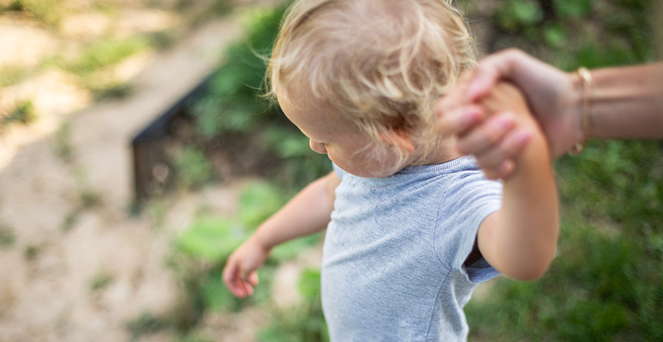 Parent holds hand of small child while walking outdoors