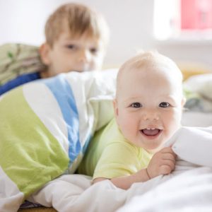 Baby girl and older brother playing on bed at home